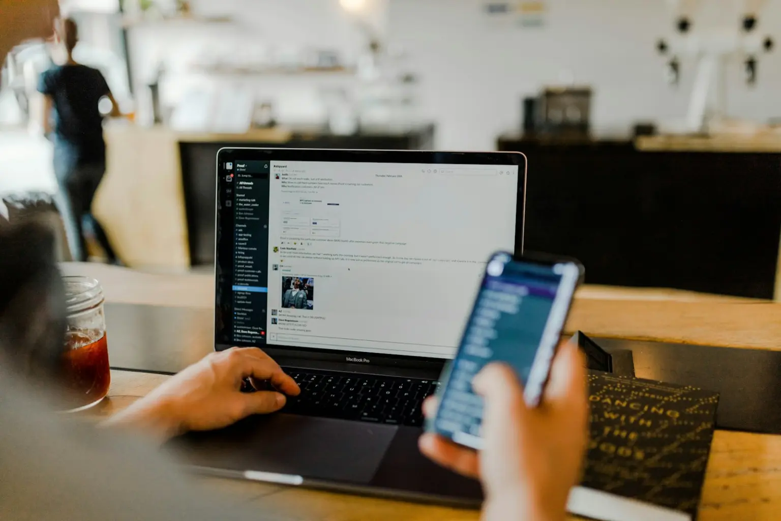 Person using a laptop and a phone at a cafe table