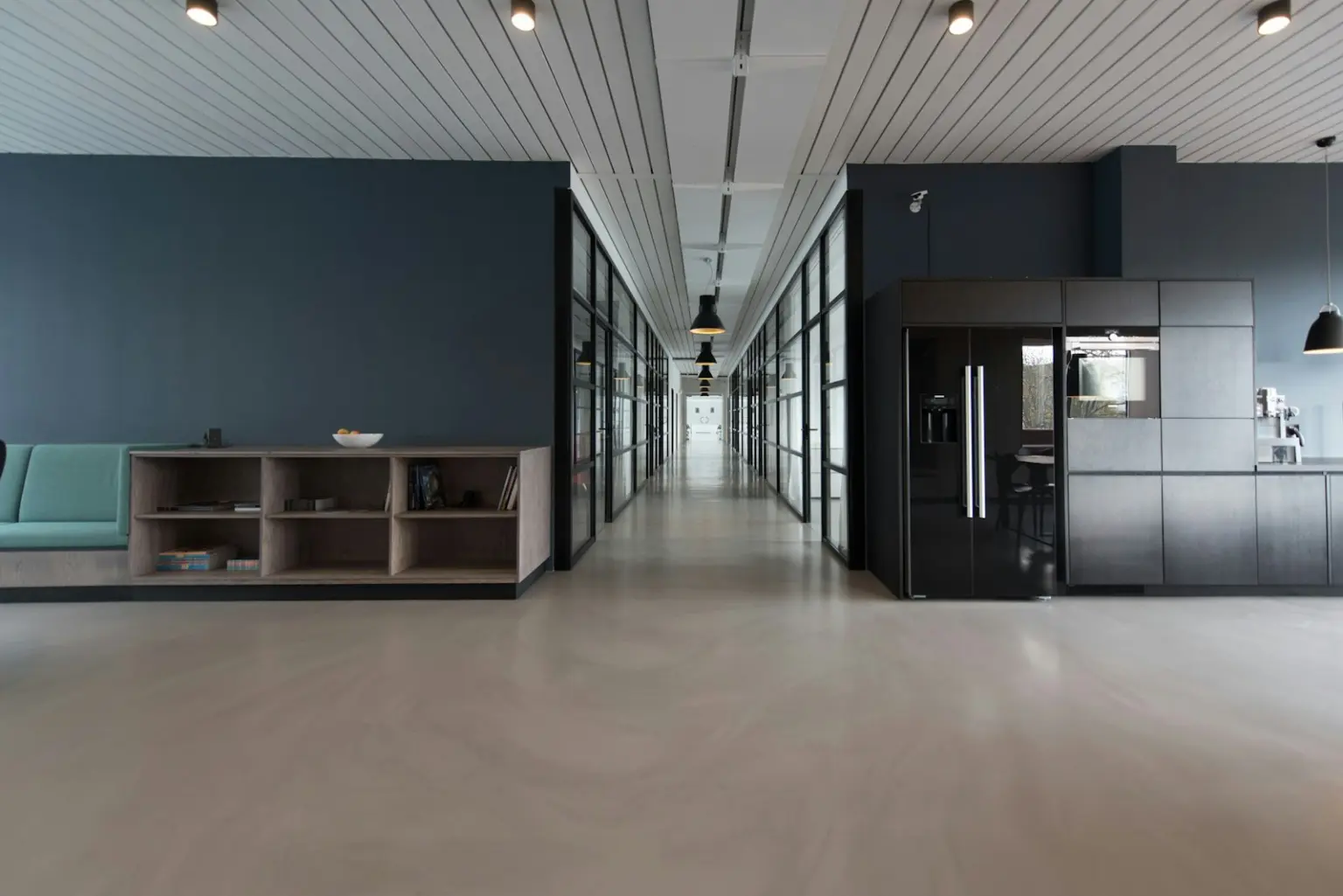 Empty modern office corridor with a kitchen area and glass meeting rooms
